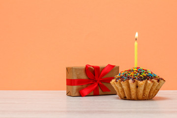 Tasty birthday muffin with burning festive candle and a gift box.