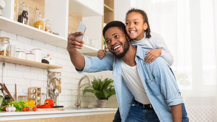 Afro dad and daughter taking selfie on cellphone in kitchen