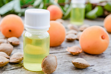 Apricot oil in a small jar near ripe yellow apricot on a wooden table.