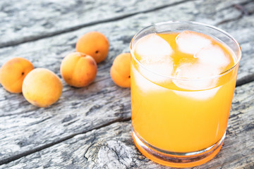 Fresh apricot juice with apricots and ice cubes in a glass against the background of old boards. Summer soft drinks.