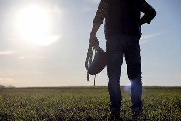 A man cowboy hat and a loso in the field. American farmer in a field wearing a jeans hat and with a loso. A man is walking across the field silhouette