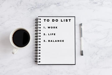 To do list work, life, balance, writing on notebook. Notebook on desk with coffee cup and a pen.