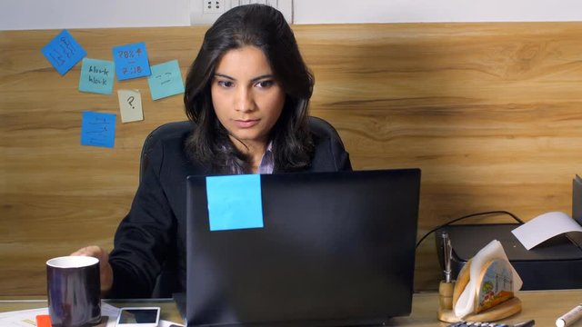 Indian girl working in office takes a sip of tea and makes weird facial expression. 