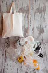 One eco-friendly cotton shopping bag hanging vs many plastic bags on a rustic wooden background