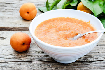 Apricot jam in a white bowl and ripe apricots on a wooden table.
