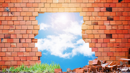 Demolished red  brick wall with a big hole in the middle with blue sky and clouds. Demolishing...