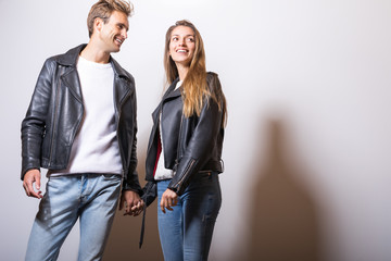 Young beautiful couple in black leather jackets pose in studio.