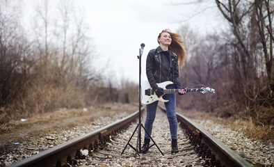 Beautiful young girl rocker with electric guitar. A rock musician girl in a leather jacket with a guitar sings. A rock band soloist plays the guitar and screams into the microphone.