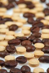 Coffee beans mixed with caffeine tablets are scattered on a light surface. Selective focus.