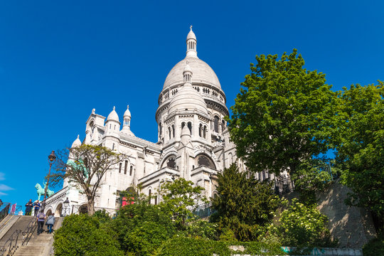 Great side view of the famous monument Sacr&eacute;-Coeur Basilica at the staircase between Rue du Cardinal Dubois and Rue Lamarck on a nice sunny day with a blue sky in Montmartre, Paris, France. 