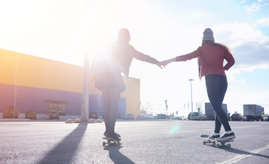 A young hipster girl is riding a skateboard. Girls girlfriends for a walk in the city with a skateboard. Spring sports on the street with a skateboard.