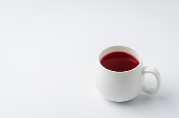 Red hibiscus tea in a white mug on a white background, copyspace