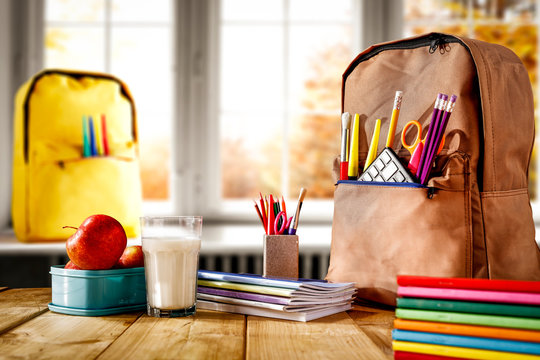 Schoolbags background with some school supplies on wooden desk top and a windowsill with white window autumn view. Empty space for product and decoration.