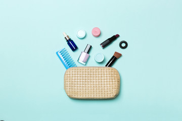 Top view of set of make up and skin care products spilling out of cosmetics bag on blue background....
