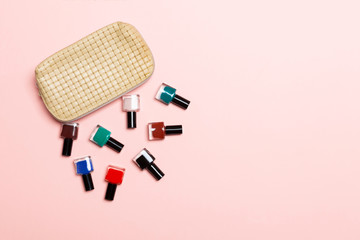 Top view of the set of nail polishes and bright gel varnishes fallen out of cosmetics bag with copy space on pink background. Trendy nail concept