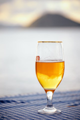 Half full glass of  beer on the table with blurred sea, sky and island background at sunset.