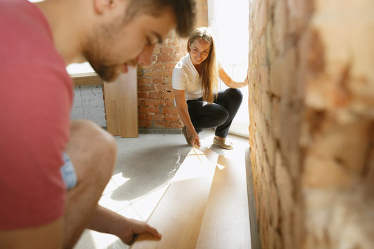 Young couple doing apartment repair together themselves. Married man and woman doing home makeover or renovation. Concept of relations, family, love. Laid laminate flooring, smiling, look happy.
