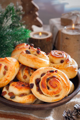 Obraz na płótnie Canvas Buns with raisins in a clay bowl with candles and winter decor, selective focus