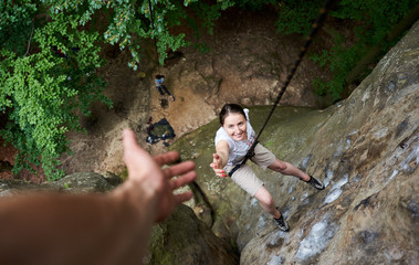 Happy woman climbing rock. Carefree hiker smiling her friend, hanging on rope and stretching out hand, asking for help. Man helping his friend to climb rock. Helping hand. Teamwork concept. Top view.