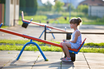 Cute young child girl outdoors on see-saw swing on sunny summer day.