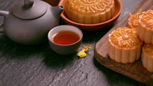 Beautiful Moon cakes on a wooden tray with tea and flower on black slate background. Chinese traditional Mid-Autumn Festival concept. Truck right.