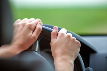 Woman hands on steering wheel driving a car.