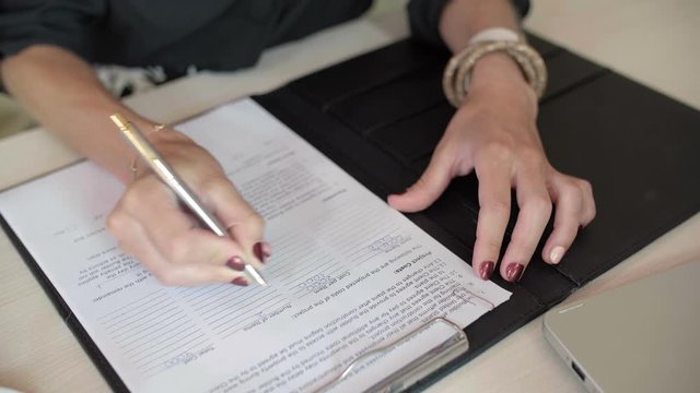 Close up of female hands holding pen and making notes in document lying on desk