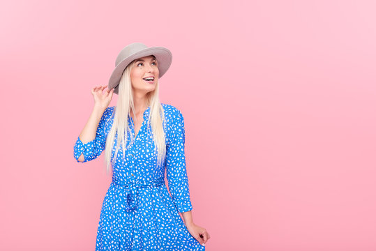 Portrait of a smiling attractive blond woman in summer hat and stylish blue dress and in braces isolated over pink background. The concept of a healthy and snow-white smile. Space for text on right