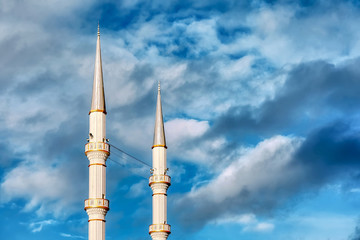 Mosque minaret, loudspeakers and ridge against a vibrant cloudy blue sky background with copyspace