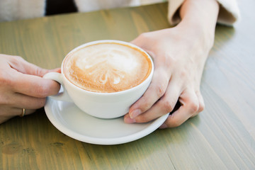 Cup of fresh cappuccino coffee in female hands on the table in summer cafe