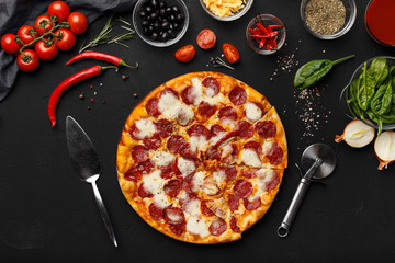 Pepperoni pizza, cooking ingredients and tools on black table