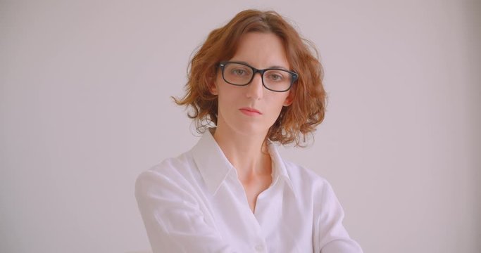 Closeup portrait of redhead caucasian businesswoman in glasses looking at camera with confidence sitting in armchair white office