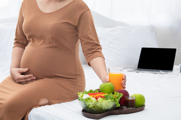 Obraz na płótnie Canvas Selective focus pregnant belly happy Asian woman eating healthy food and orange juice sit on bed at home