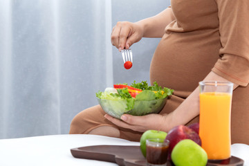 Obraz na płótnie Canvas Selective focus pregnant belly happy Asian woman eating healthy food and orange juice sit on bed at home