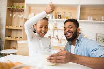 Fototapeta na wymiar Cute afro girl making dough with her father, having fun