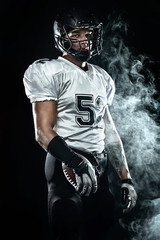 Fototapeta na wymiar American football sportsman player in helmet on black background with smoke. Sport and motivation wallpaper.