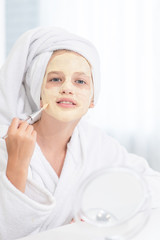 Smiling girl in towel on her head  make a clay facial mask at home