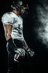 American football sportsman player in helmet on black background with smoke. Sport and motivation...