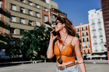 Fototapeta premium Beautiful young caucasian woman walking at the city street on a sunny day. Talking on mobile phone. Happy face smiling. Urban lifestyle
