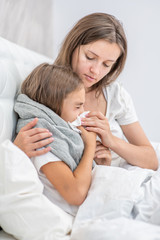 Mother on the bed blowing the nose of her little girl