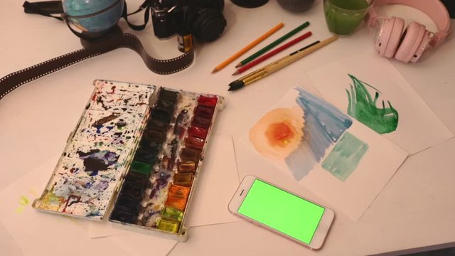close up smartphone on table with art objects watercolor brush studio art home loft 5g green screen chroma key social technology media