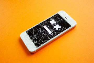 Broken smartphone with cracked destroyed screen on orange background with sad smile. Broken phone...