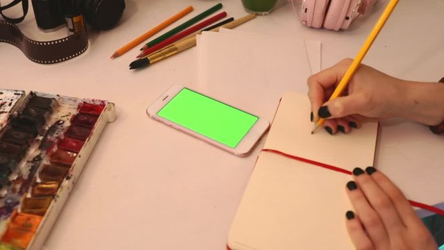 student painting from smartphone on table with art objects watercolor brush studio home loft 5g green screen chroma key social technology media study design tutorial illustrator work freelance