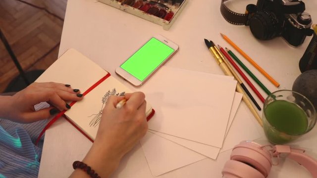 close up girl painting from smartphone on table with art objects watercolor brush studio home loft 5g green screen chroma key social technology media study design tutorial illustrator work freelance