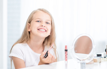 Smiling girl paints lips in front of a mirror at home