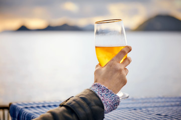 Close up hand of a woman holding a glass of beer with blurred sea, sky and island background at...