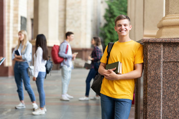 Happy teen guy holding books and smiling in college campus