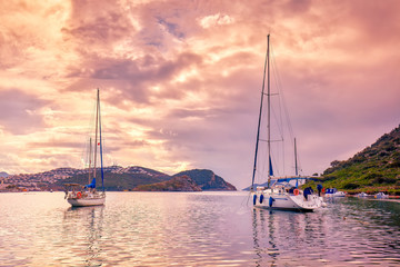 Yachts anchored over the calm sea at sunset in gumusluk bay in Bodrum, Mugla, Turkey.