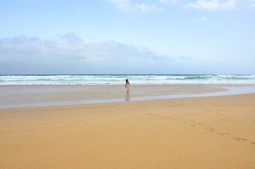 Fototapeta na wymiar Girl Wearing a Dress Walking by a Long Sand Beach in Fuerteventura, Canary Islands