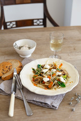 Mixed vegetable stir fry with mushrooms and cottage cream cheese. Tender mushroom stir fry served in a white plate with white wine and bread on the wooden table. Vegan food